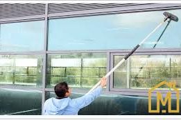 Un homme nettoie une fenêtre avec un long nettoyeur.