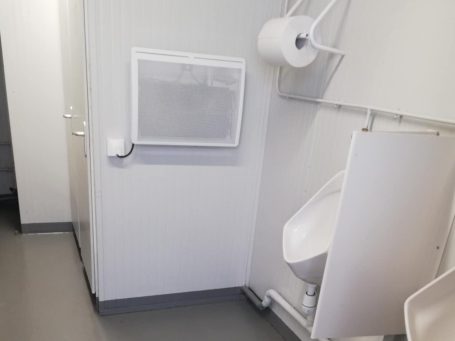 Cabine de toilettes avec un urinoir et un distributeur de papier toilette.