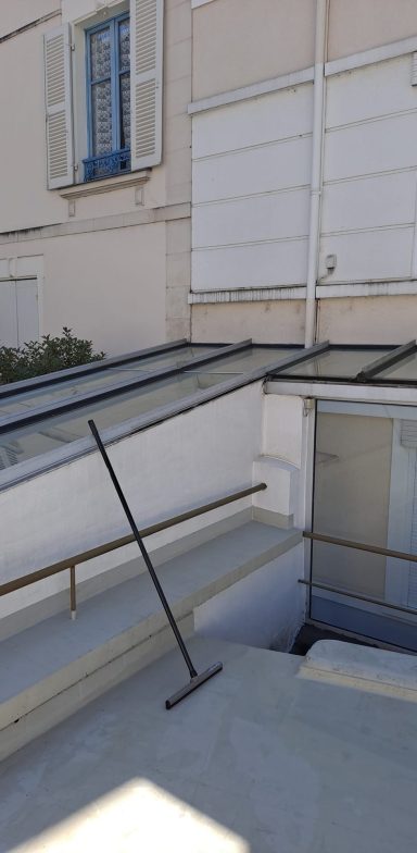 Rampe d'accès avec un balai reposant sur une surface inclinée près d'une entrée.