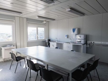 Salle de réunion moderne avec une grande table, chaises et équipements de cuisine.