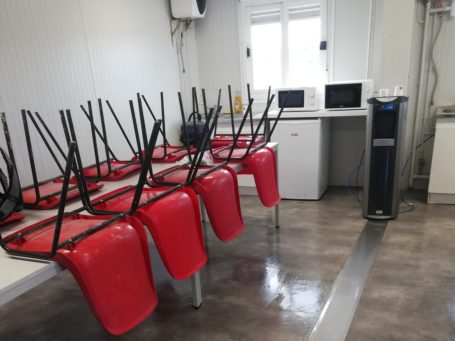 Salle avec des chaises rouges retournées sur des tables, un micro-ondes et un climatiseur.